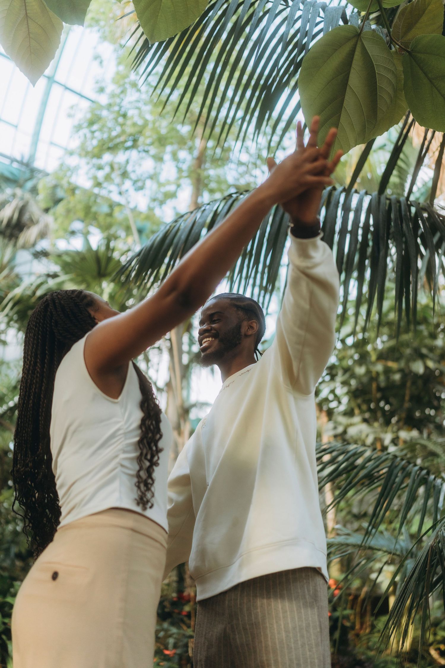 A joyful couple dances together in a tropical greenhouse setting.