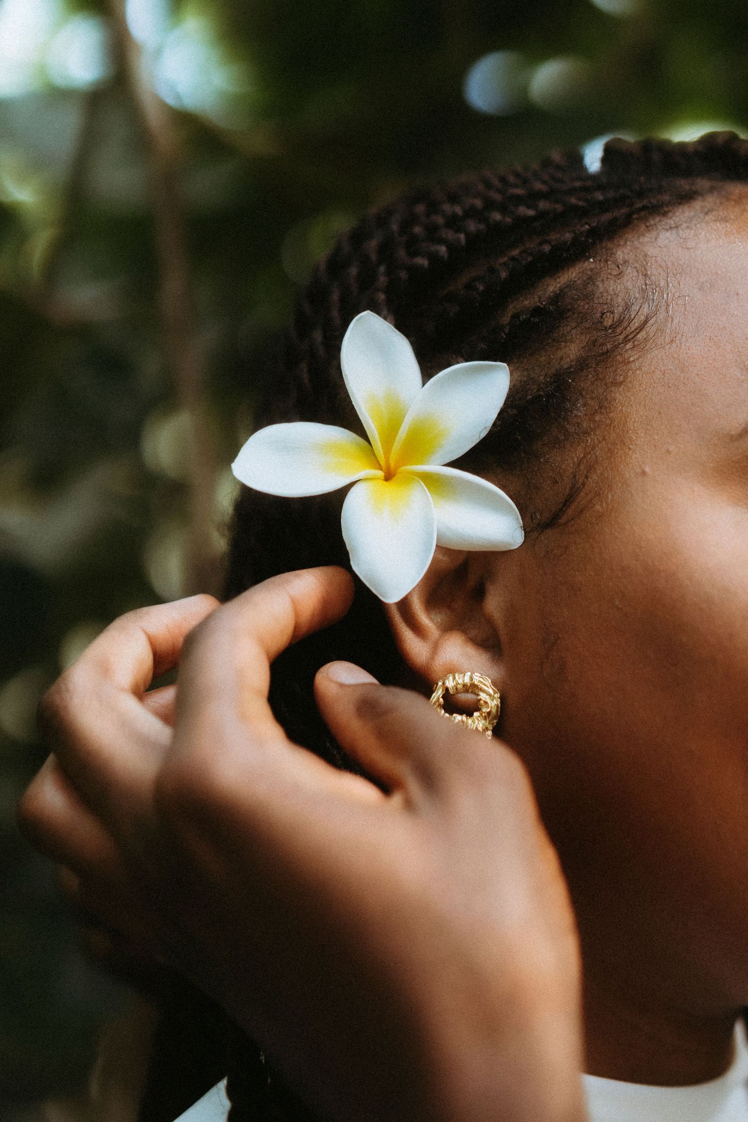 A delicate white plumeria flower adorns braided hair in a close-up shot.