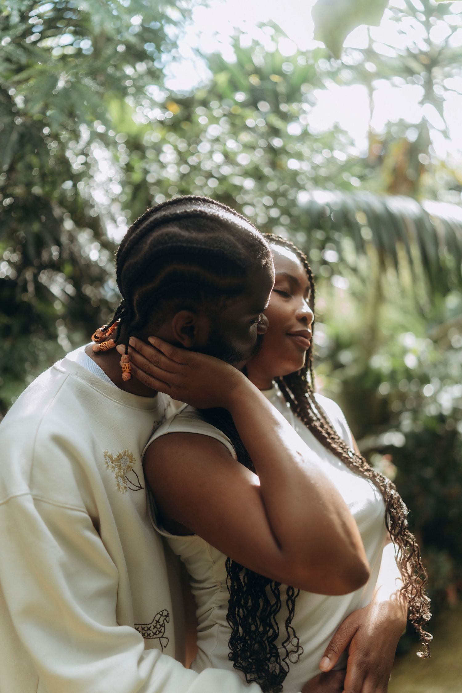 A couple shares a romantic embrace among tropical plants in a greenhouse.