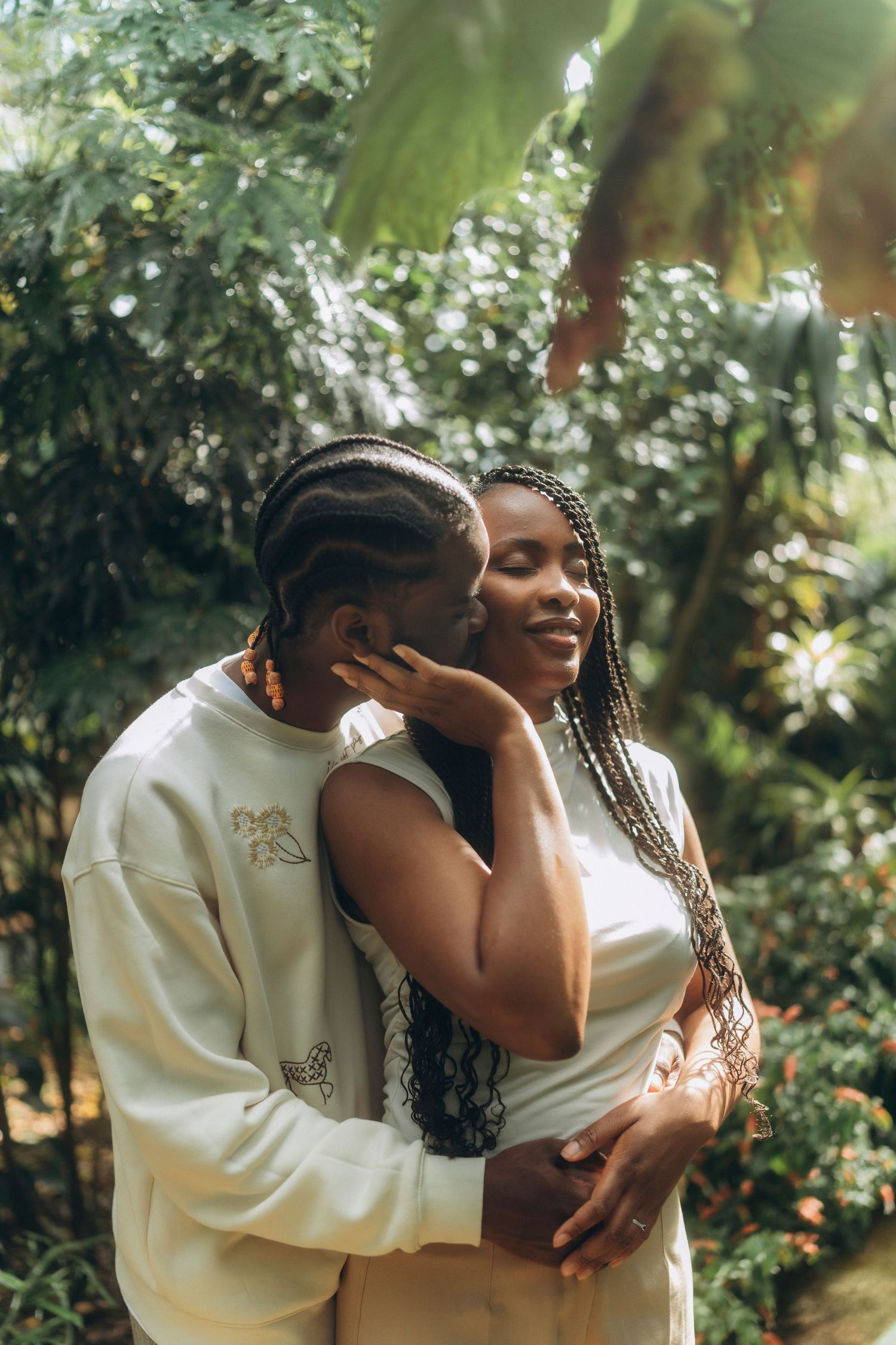 A loving embrace captured in a sunlit greenhouse surrounded by tropical foliage.