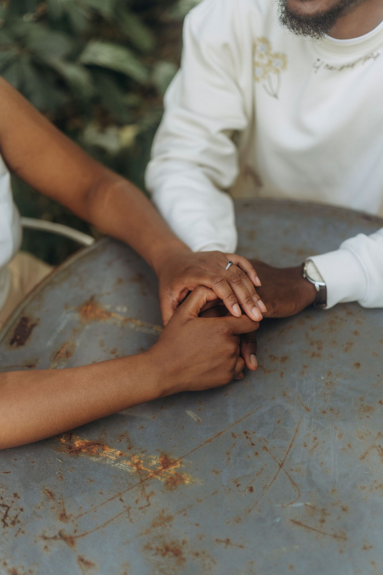 Two hands tenderly intertwined on a rustic metal table surface.