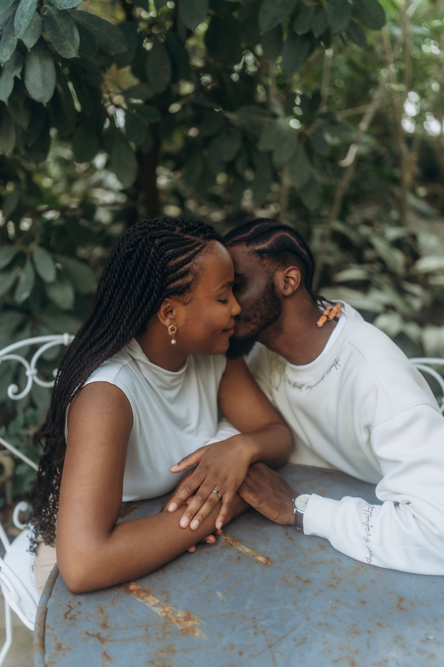 An intimate moment shared between a couple at a metal table in a garden setting.