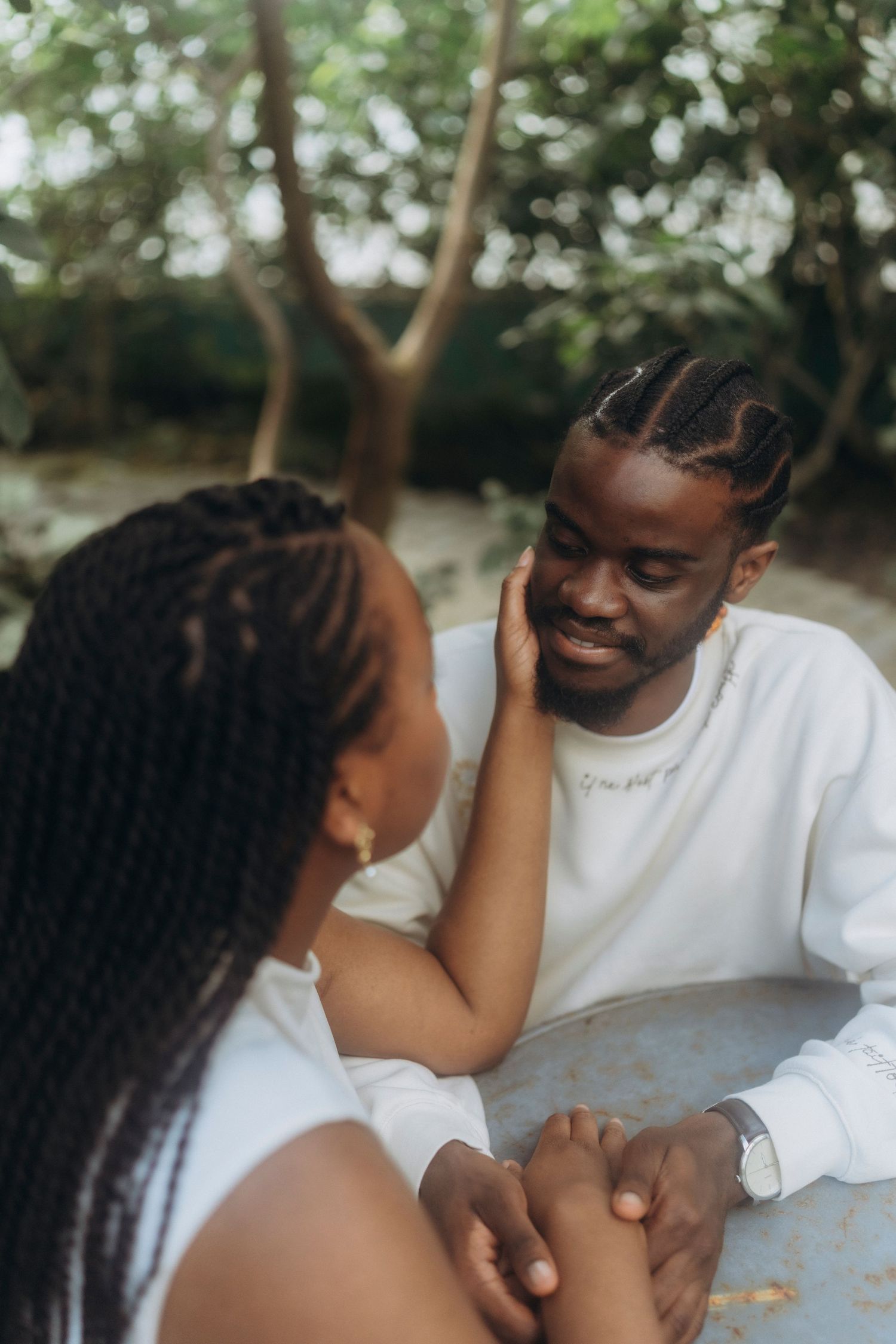 Couple sharing an intimate moment at an outdoor table with natural foliage in the background.