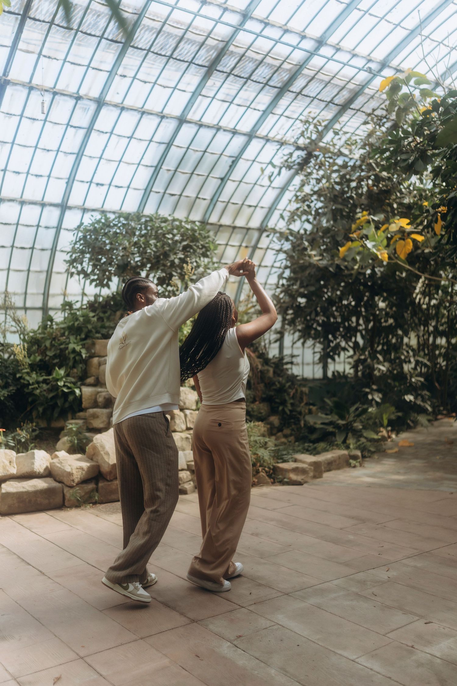 Dancing couple in a light-filled greenhouse with glass ceiling and tropical plants.