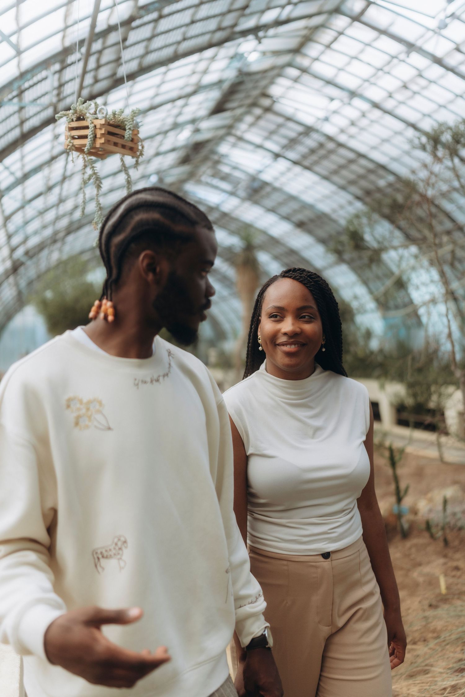 Couple walking together in a beautiful greenhouse with glass ceiling and natural lighting.