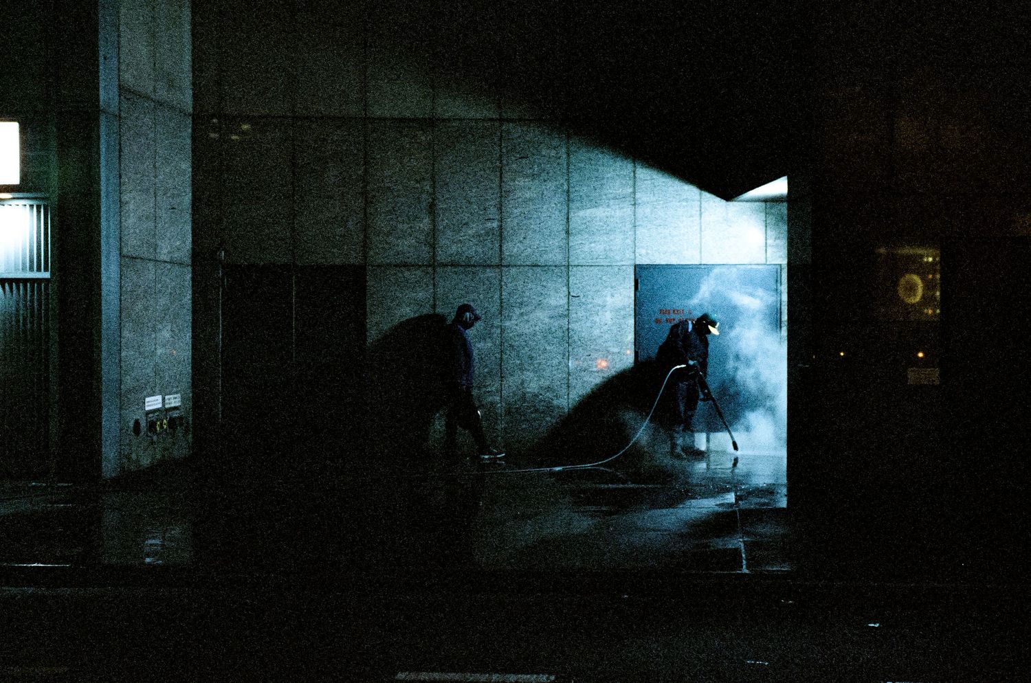 Silhouettes of people in a dimly lit concrete space with moody blue lighting.