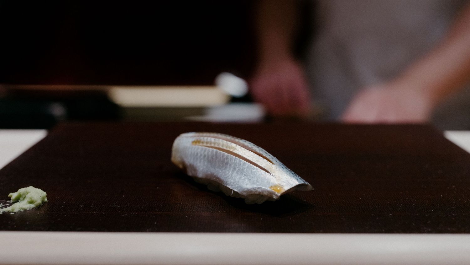 Fresh slice of raw fish prepared for sushi placed on a dark wooden surface.