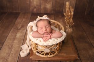 Sleeping newborn baby posed in rustic wooden props with soft lighting and neutral tones.
