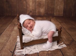 Newborn baby sleeping on white lace blanket with rustic wooden floor backdrop.