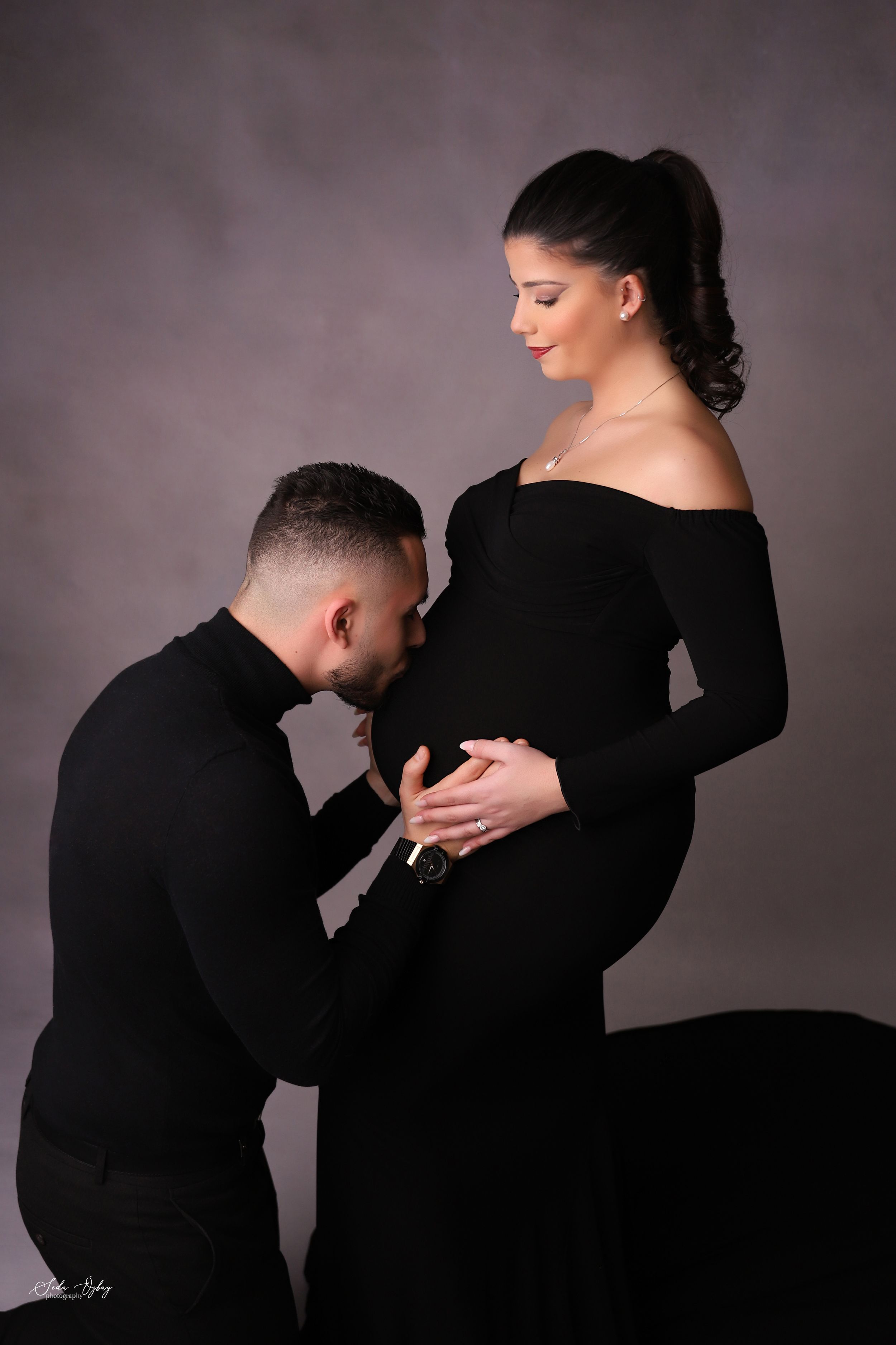 Intimate maternity portrait with couple in black attire against muted background.