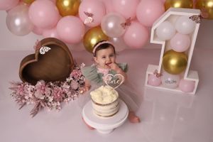 Pink and gold balloon garland with floral decorations and cake display for a celebration.