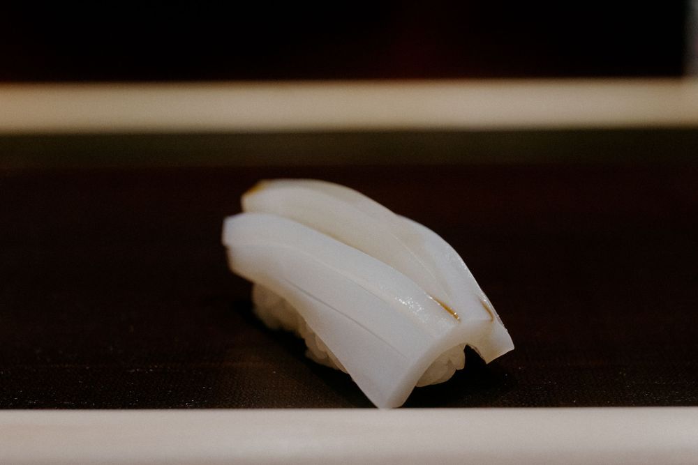 Fresh slices of white fish sushi arranged on a black surface with delicate knife cuts.