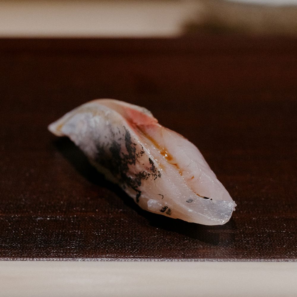 A single piece of mackerel nigiri sushi displayed on a dark surface.