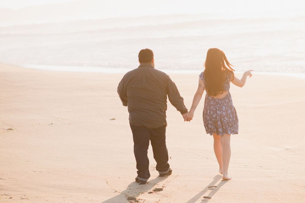 A couple walking hand in hand on a sandy beach during golden hour.