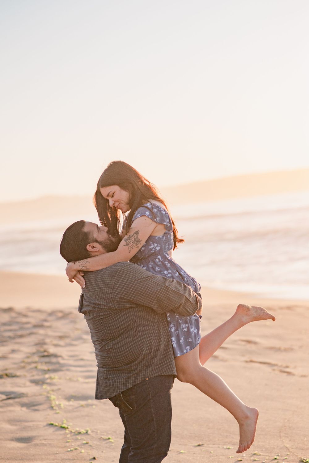 A playful couple embracing on the beach during sunset.