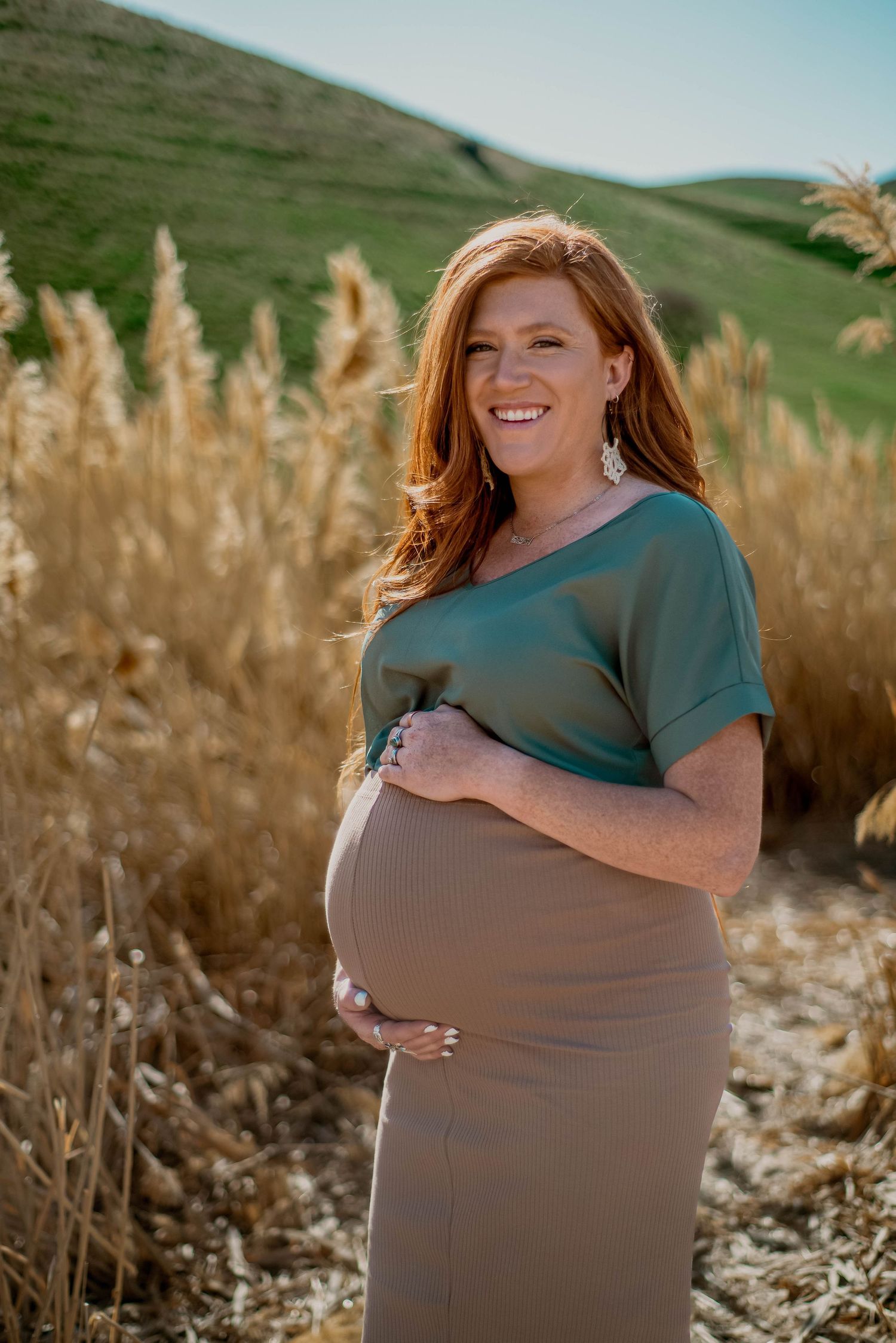 Maternity portrait in green dress against golden grass and rolling hills background.