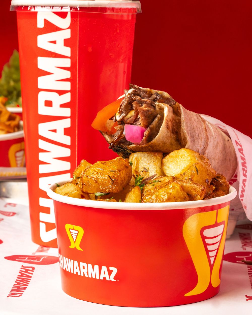 A fast-food meal with a wrapped sandwich, roasted potatoes and red beverage cup displaying Shawarmaz branding. Mtlshutter photography