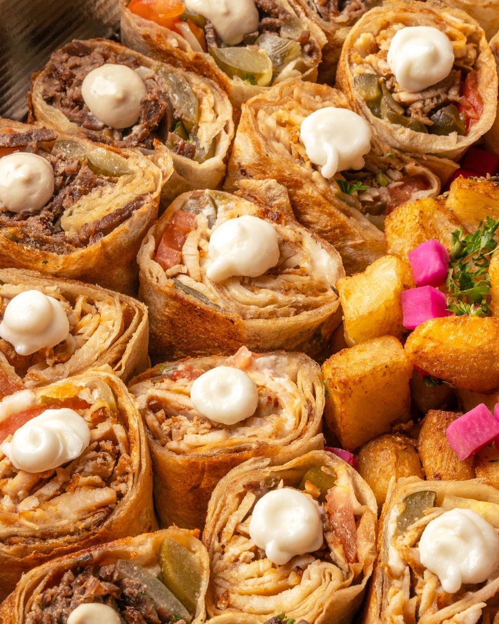 Close up of shawarma wrap slices topped with white sauce and served with colorful pickled vegetables. Mtlshutter photography