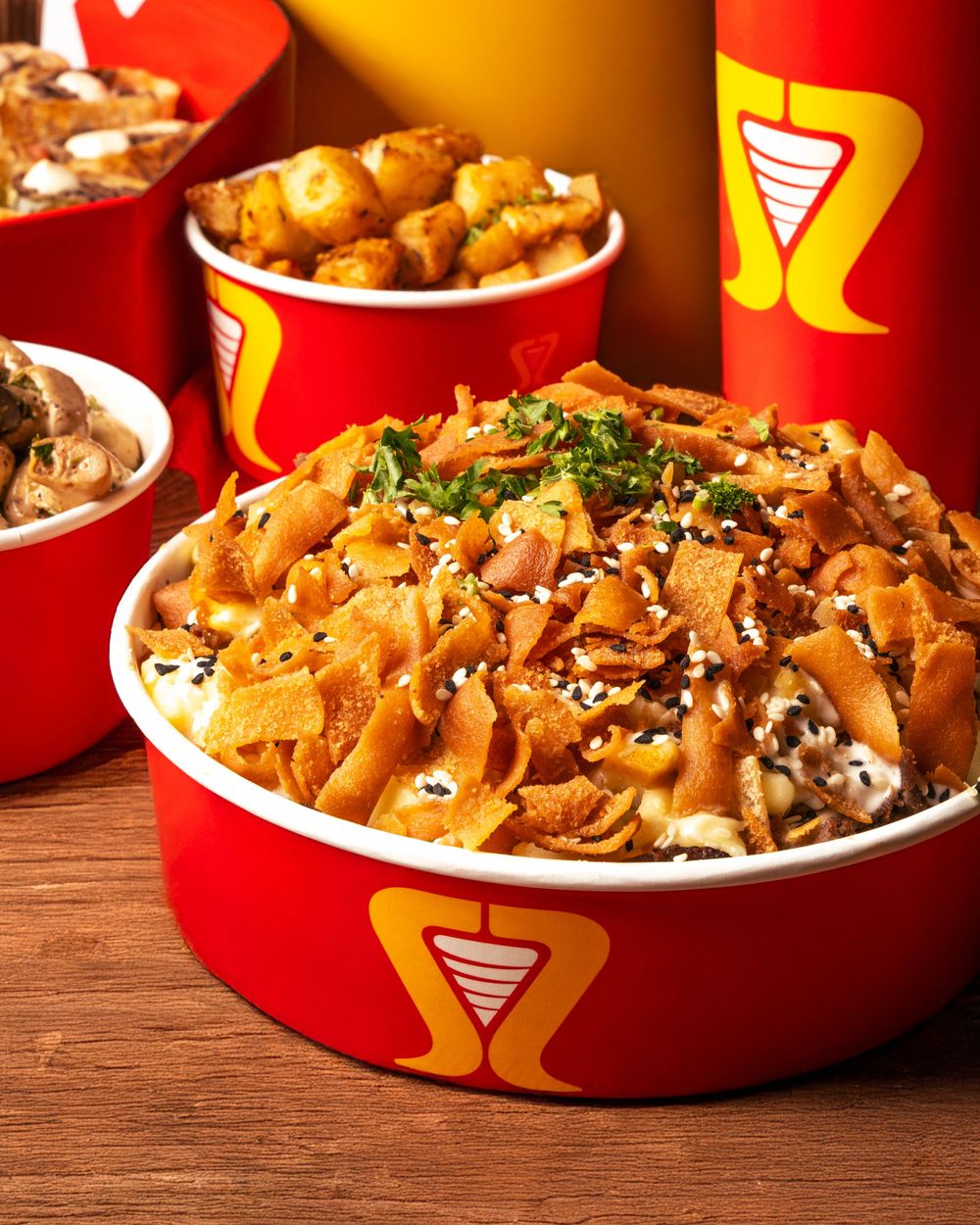 Large bowl of sesame-topped noodles with sides in red branded containers on wooden surface. Mtlshutter photography