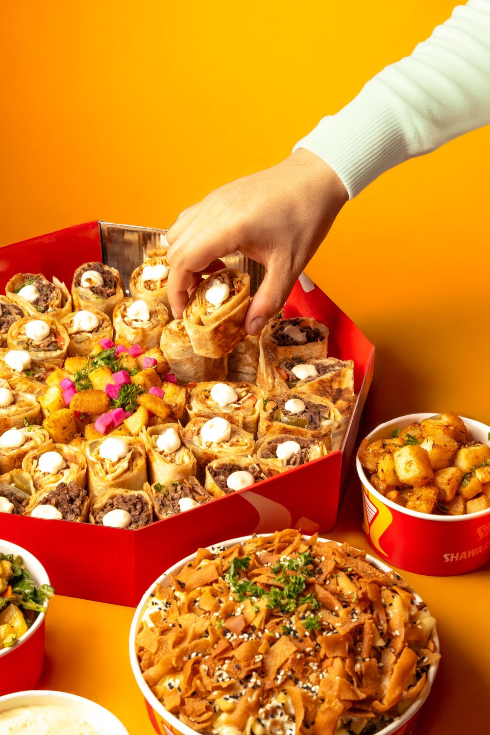 Overhead view of Middle Eastern platters with wraps and potatoes arranged on an orange background. Mtlshutter photography