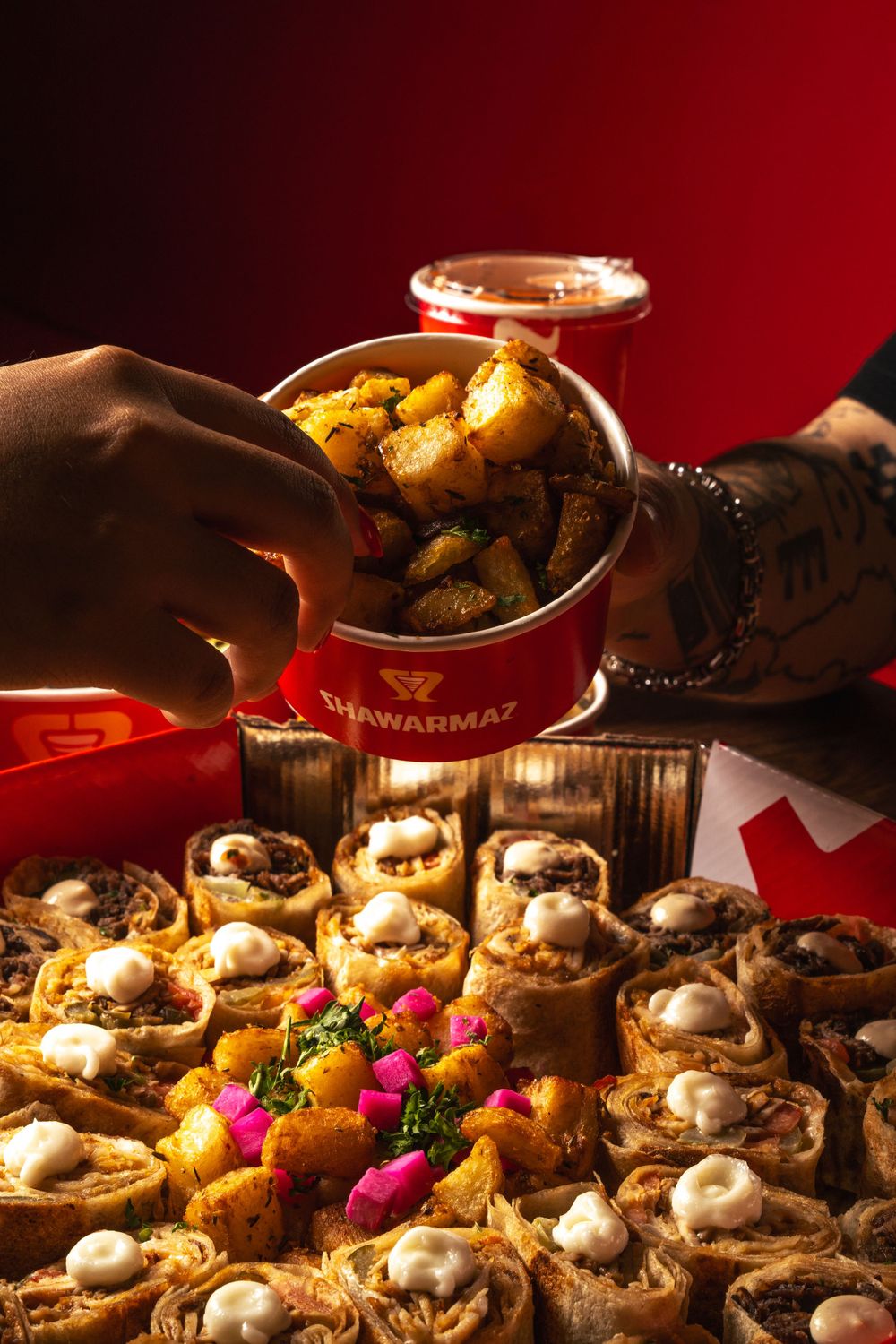 Festive spread of Middle Eastern wraps and roasted potatoes with hands reaching for food in dim lighting. Mtlshutter photography