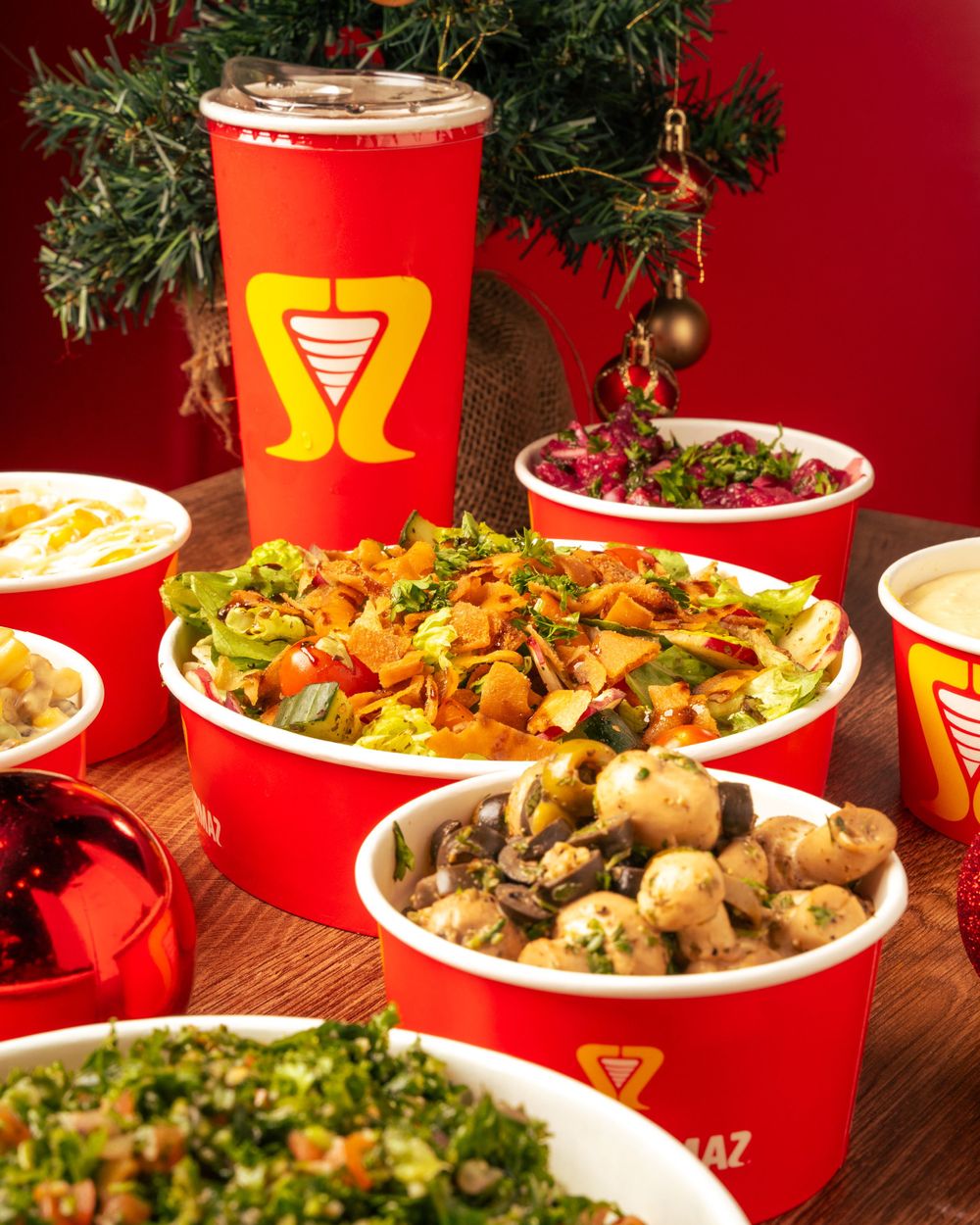 Holiday-themed display of Middle Eastern dishes in red bowls with Christmas decor and branded cups. Mtlshutter photography