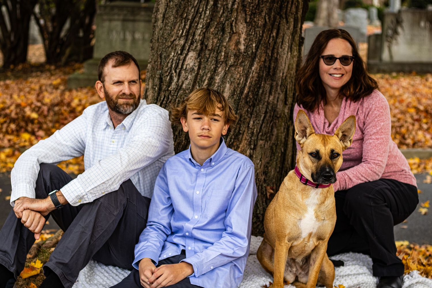 Family sits together on autumn ground with their brown dog while surrounded by fallen leaves.