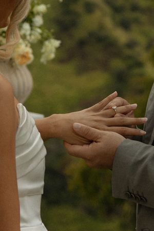 Close-up of hands exchanging wedding rings during an outdoor ceremony.
