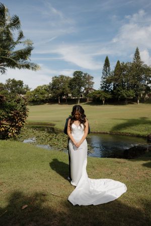 A bride in a white wedding gown stands by a pond on a lush golf course.