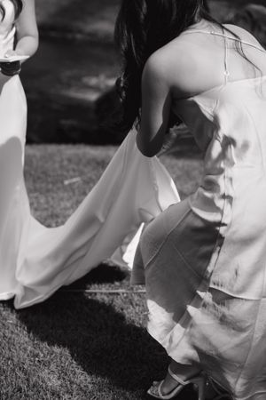 A black and white detail shot of a wedding dress being adjusted outdoors.