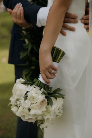 Close-up of white wedding bouquet and bridal dress details showing elegant ring and wrapped stems.