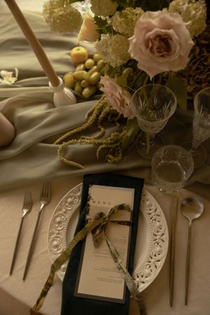 Elegant wedding place setting with pink roses and detailed menu card on white linens.