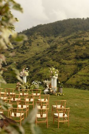 An outdoor wedding ceremony setup with wooden chairs and floral arrangements against a mountain backdrop.