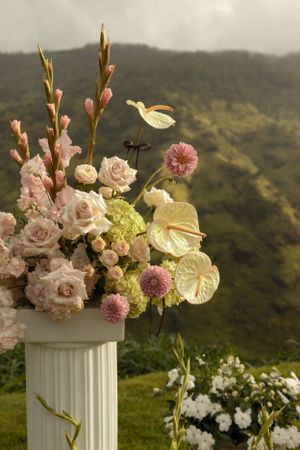 Stunning floral arrangement with pink roses and anthurium on a white column with mountain views.
