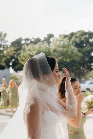 A bride in a white veil and wedding dress stands outdoors with emotional gestures during the ceremony.