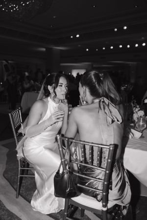 Two people in formal attire share an intimate conversation at an elegant reception with string lights overhead.