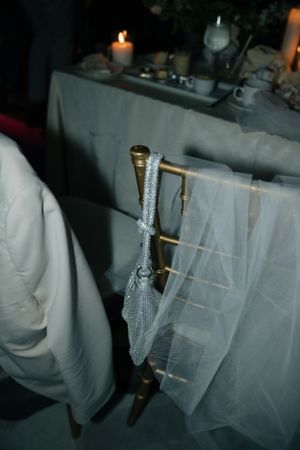 A white wedding veil drapes elegantly over a silver glitter-covered vertical stand with candlelight in the background.