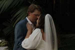 Intimate wedding moment captured against tropical foliage background.