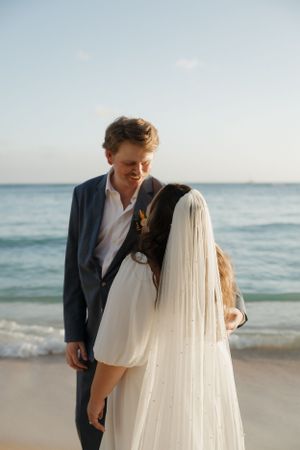 Romantic beachside wedding portrait with ocean waves and clear sky in background.