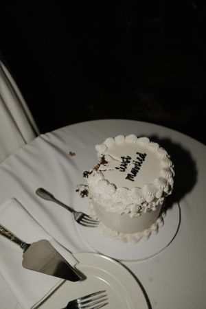 Small white wedding cake with minimal decoration photographed on white tablecloth.