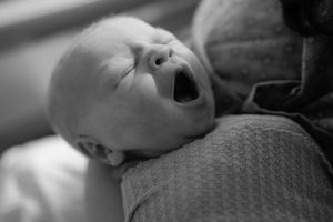 Grayscale image of sleeping newborn swaddled in textured fabric.