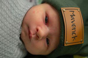 Infant wearing a knit beanie with text label while resting on textured gray fabric.