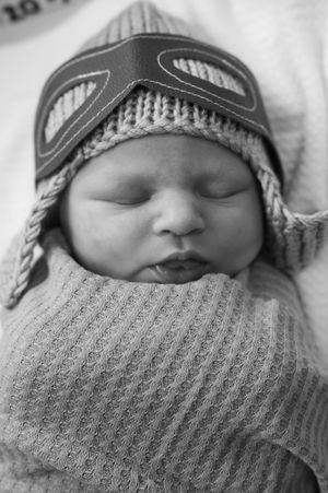 Close-up profile of sleeping newborn wearing knit beanie and wrapped in ribbed blanket.