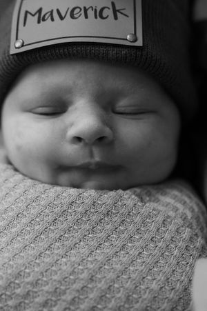 Black and white portrait of sleeping infant wearing knit hat against textured blanket.