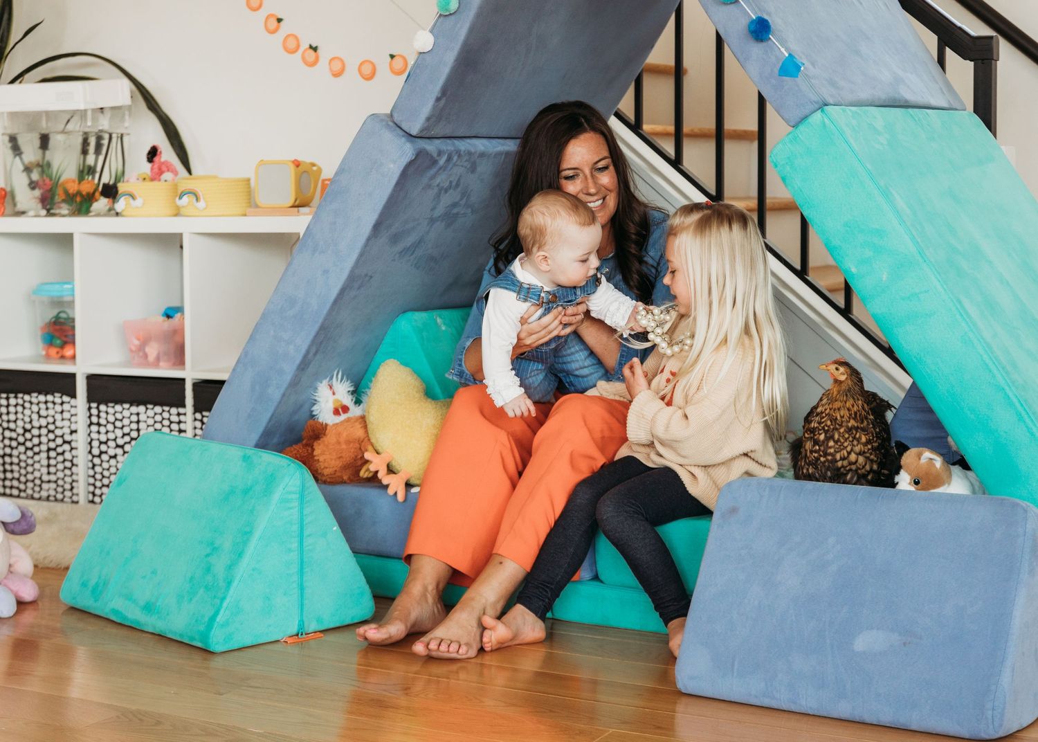 Two people relax in a cozy play tent with colorful cushions and toys while sharing quality time together.