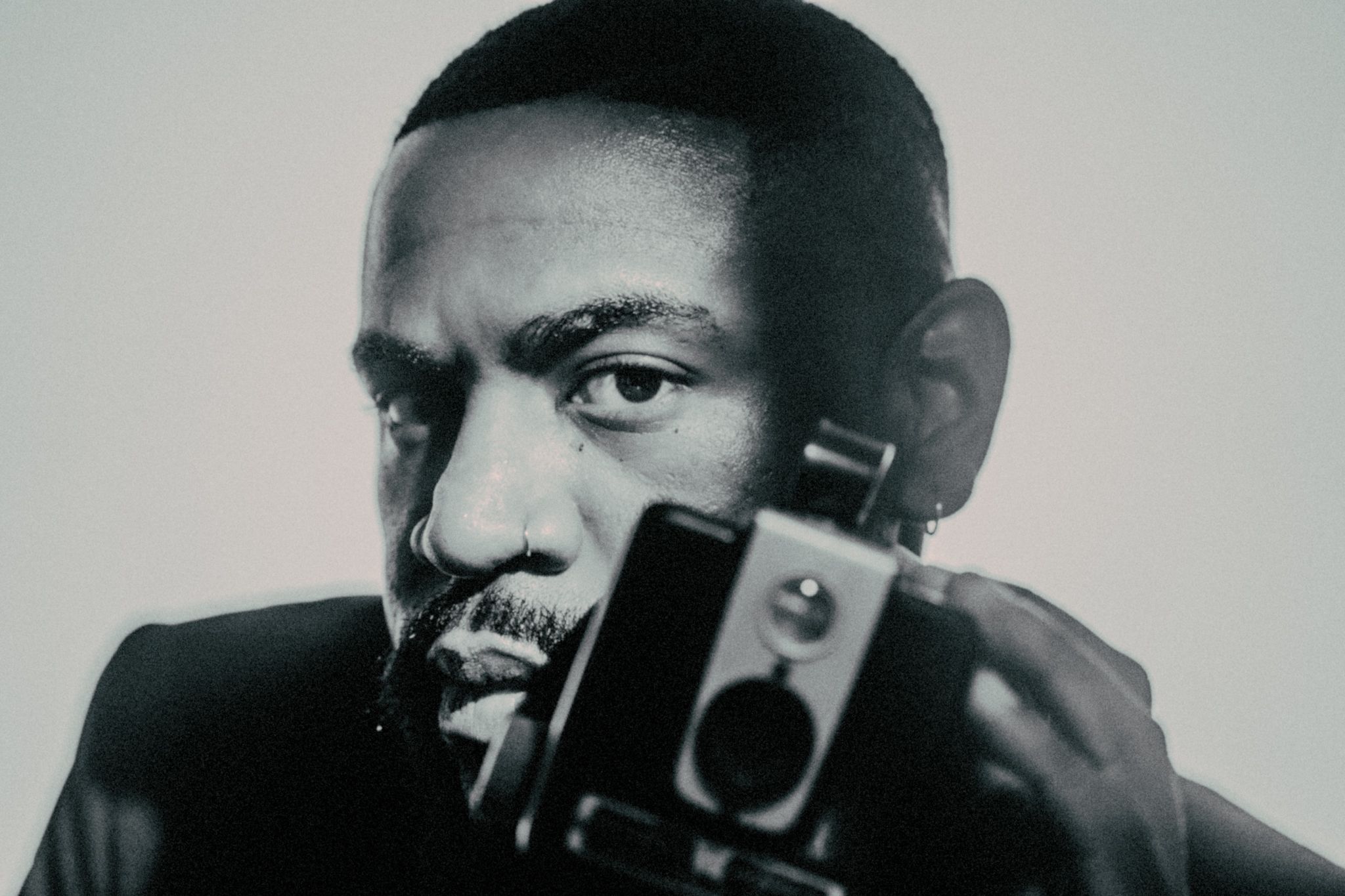 Moody studio portrait of a creative professional holding a camera in a leather jacket and jeans.