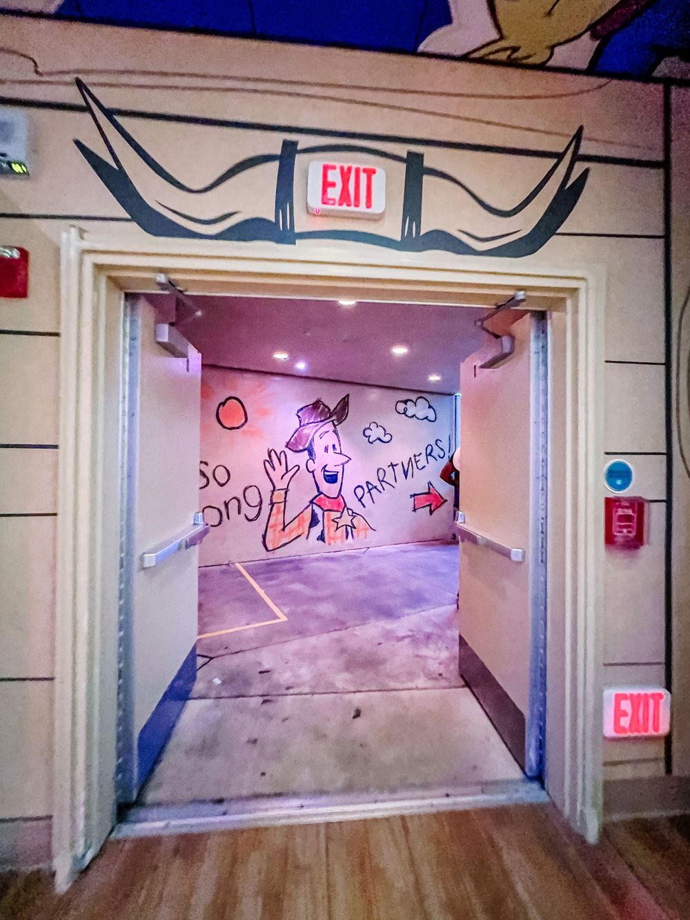 An exit doorway with neon sign and decorative wall art leads to a pink-lit hallway with graffiti-style drawings.
