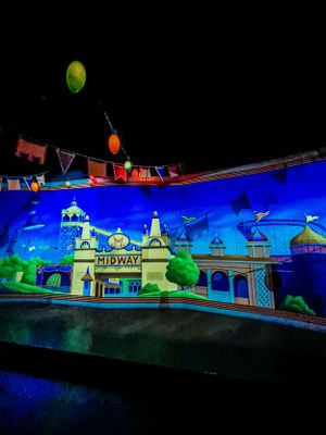 Illuminated carnival midway attractions glow with neon blue and green lights against a dark night sky.
