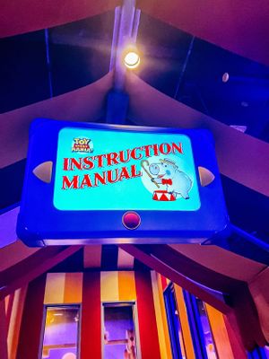 A glowing blue-lit Toy Story instruction manual sign mounted on a colorful indoor ceiling with dramatic lighting.