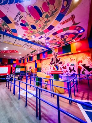 Colorful indoor arcade space with blue queue barriers and neon lights illuminating the ceiling in vibrant pink and purple hues.